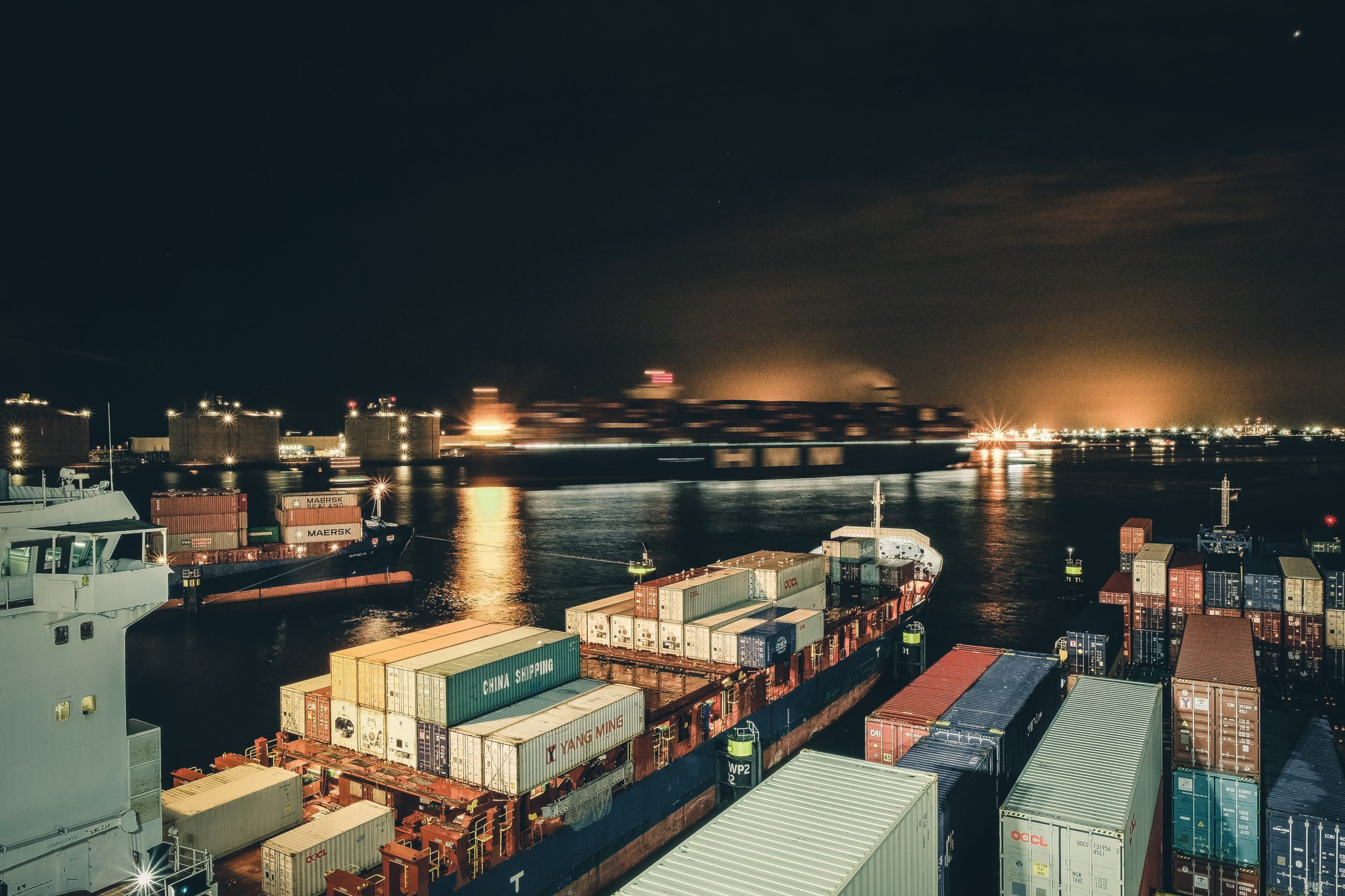 Cargo ships covered in shipping containers sit in the water at night.